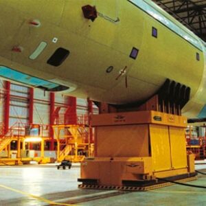 A yellow airplane in an industrial setting with some equipment.