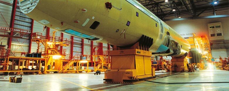 A yellow airplane in an industrial setting with some equipment.